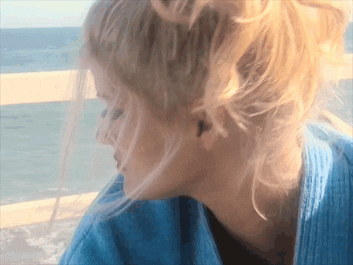 a close up of a woman 's face with the ocean behind her