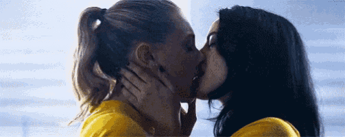 two women are kissing each other in front of a blue sky .