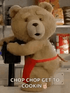 a teddy bear wearing a red apron is standing in a kitchen holding a blender .