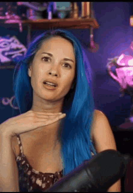a woman with blue hair is standing in front of a microphone and making a funny face .