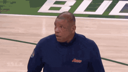 a man stands on a basketball court wearing a blue shirt that says axerv