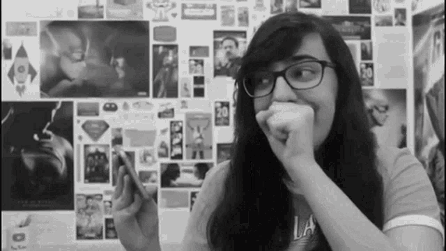 a woman wearing glasses is covering her mouth while holding a phone