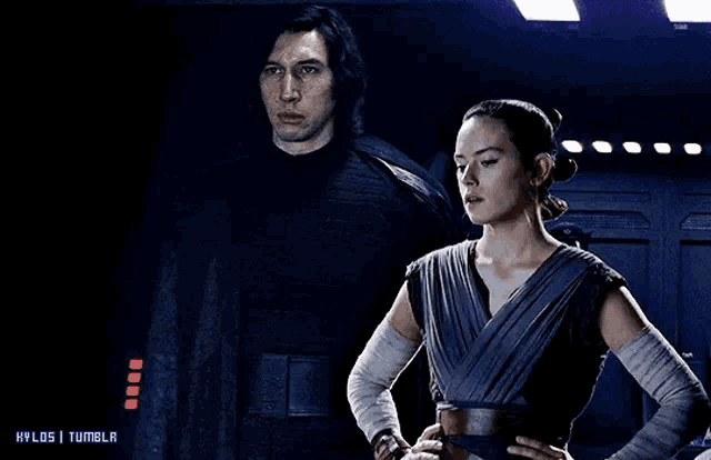 a man and a woman are standing next to each other in a dark room with their hands on their hips .