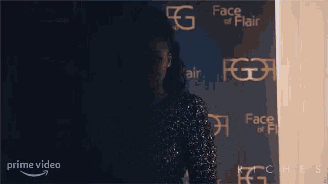 a woman stands in front of a wall with face of flair written on it