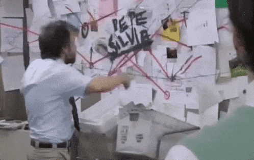 a man is pointing at a bulletin board with the name pepe silvia written on it .