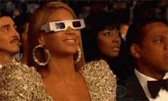 a woman wearing 3d glasses is smiling while sitting in a crowd of people