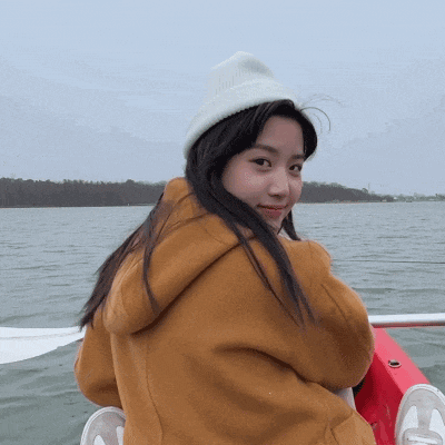 a girl wearing a white hat and a brown jacket is sitting on a boat