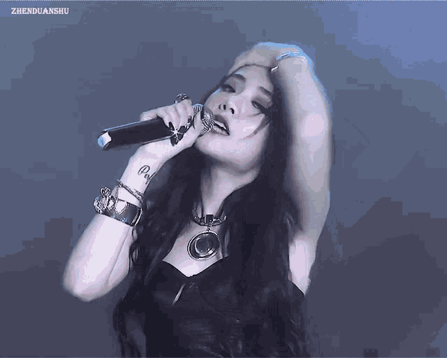 a woman with a tattoo on her wrist singing into a microphone with zhenguanshu written on the bottom right