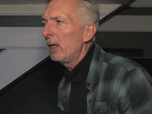 a man in a plaid shirt and black turtleneck is talking