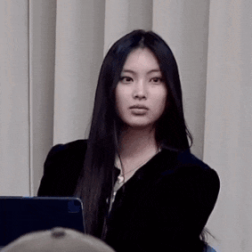 a young woman with long black hair is sitting in front of a white curtain and looking at the camera .