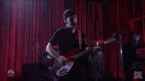 a man is playing a guitar on a stage with a red curtain in the background .