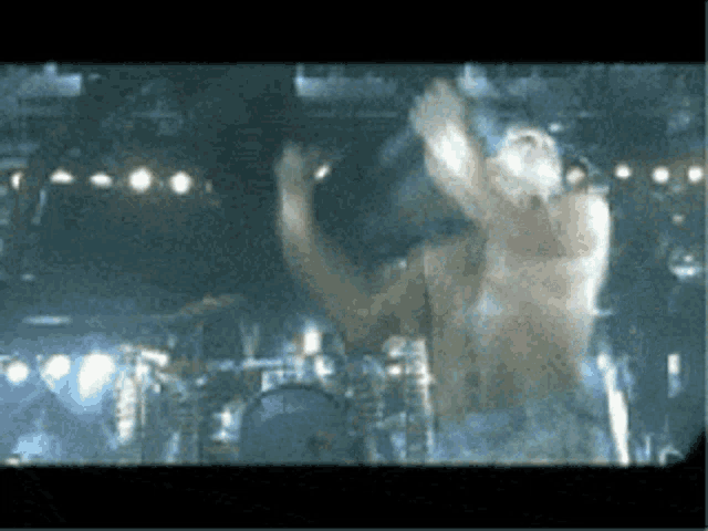 a man without a shirt is standing on a stage with a drum set in the background