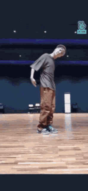 a man in a gray shirt and brown pants is standing on a wooden floor