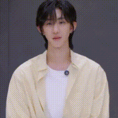a young man wearing a white shirt and a yellow jacket is standing in front of a black background .