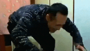 a man is kneeling down in a room with a bottle of liquid on his back .
