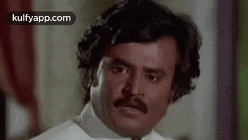 a man with a mustache and curly hair is looking at the camera .