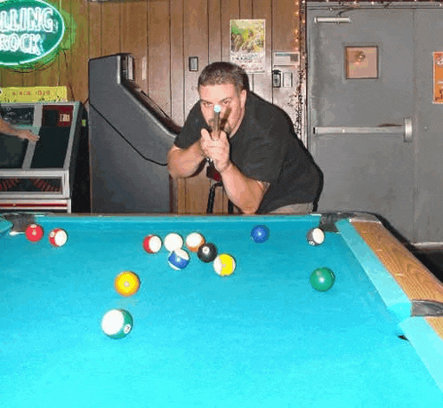 a man is playing pool on a pool table with a rolling rock sign in the background