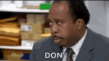 a man in a suit and tie is sitting in front of a shelf and saying `` don '' .