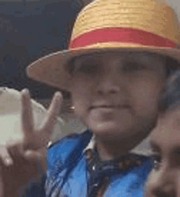 a man wearing a hat and a blue vest is giving a peace sign .