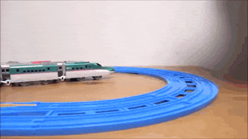 a green toy train is going around a blue track