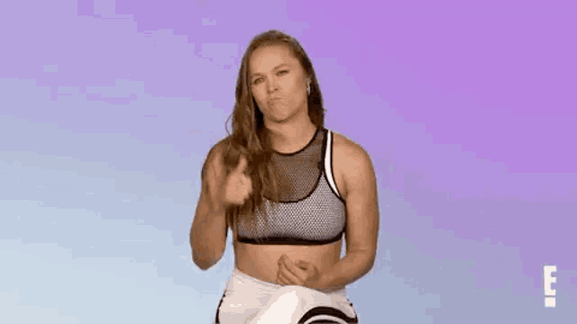 a woman in a sports bra and white pants is giving a thumbs up sign .