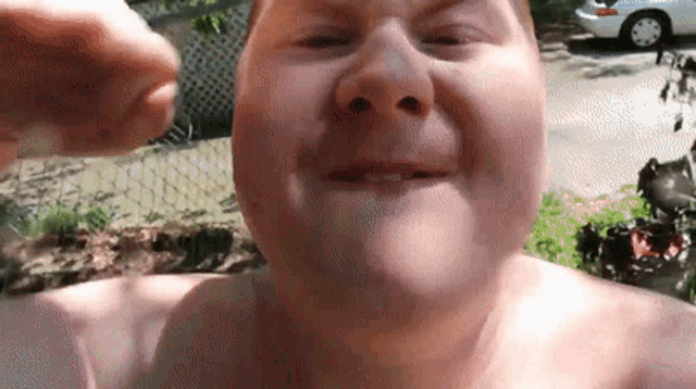 a shirtless man is making a funny face in front of a white car .