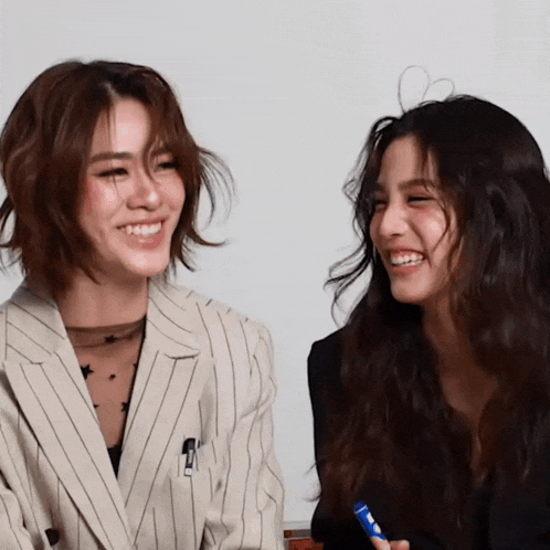 a woman with a pen in her pocket smiles next to another woman