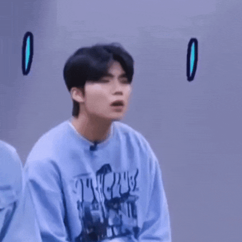 a young man in a blue sweatshirt is making a surprised face with two exclamation points above his head .