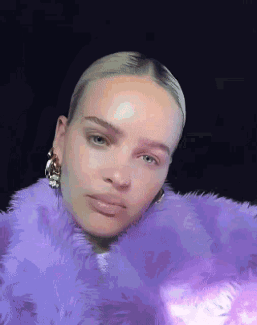 a woman is wearing a purple fur coat and earrings .