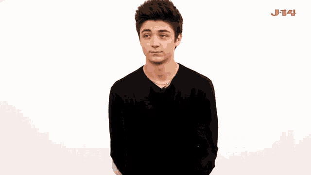 a young man in a black shirt is dancing in front of a white wall with the letters j-14 on it