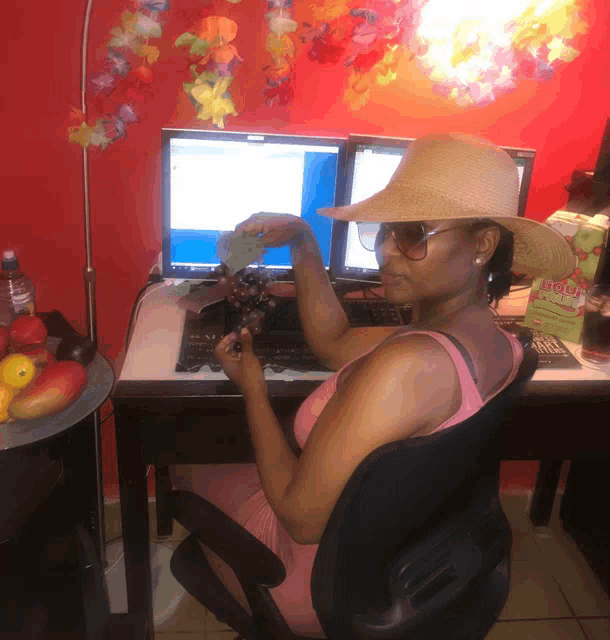 a woman wearing a straw hat is sitting at a desk with two computers