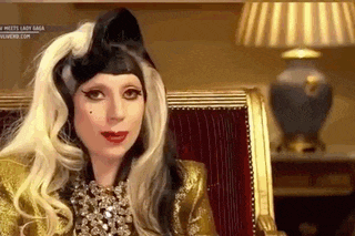 lady gaga is sitting in a chair wearing a wig and a hat .