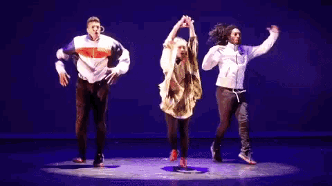 a group of three people are dancing on a stage with a blue background