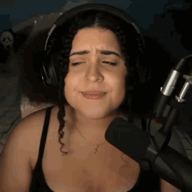 a woman wearing headphones stands in front of a microphone with her eyes closed