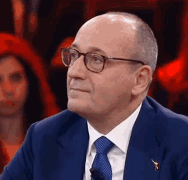 a man wearing glasses and a blue suit looks to his left