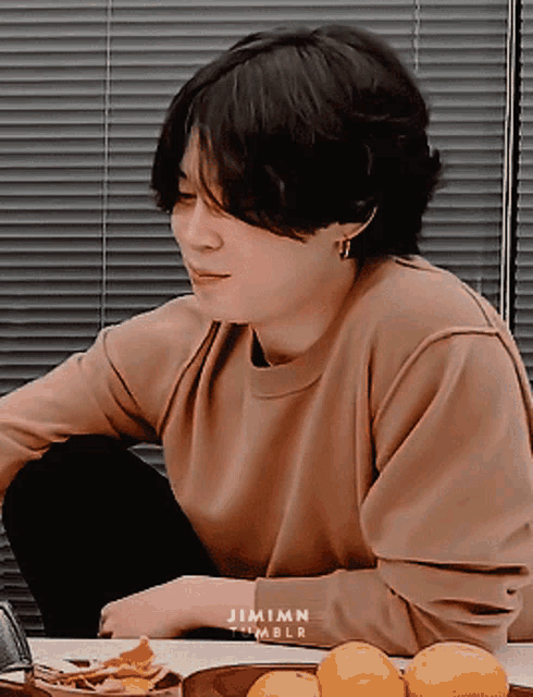 a man in a brown sweater sits at a table with oranges