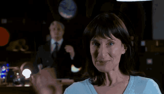a woman in a blue sweater smiles and waves her hand