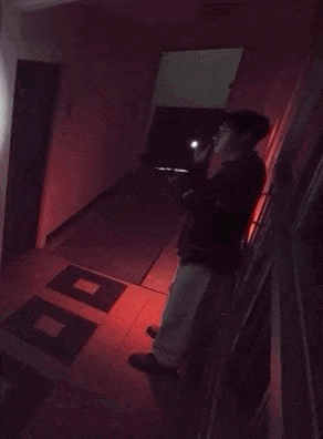 a person is sitting on a railing in a dark room with a red light shining on the floor .