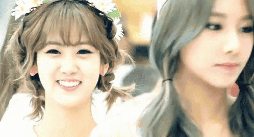 two girls are standing next to each other and smiling for the camera . one of the girls has a flower crown on her head .