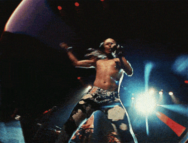 a shirtless man is singing into a microphone on stage