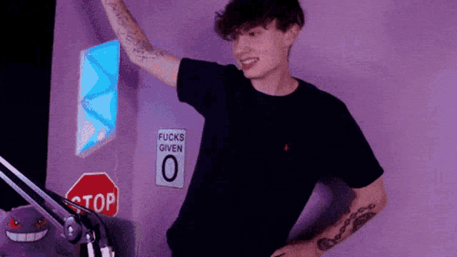a young man stands in front of a stop sign and a sign that says fucks given 0