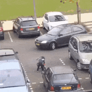 a child is riding a bike in a parking lot with cars parked in a row .