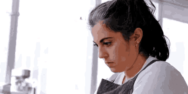 a woman in an apron is looking down at something while sitting at a table .