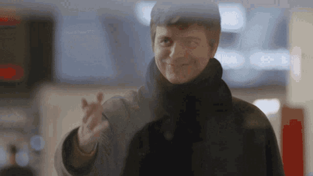 a woman in a black coat is smiling and waving her hand