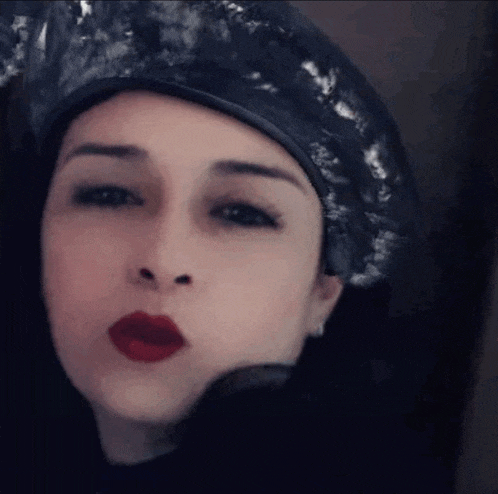 a woman wearing a black hat and red lipstick is making a kiss .