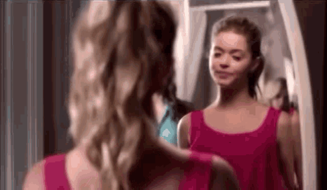 a woman in a pink dress is looking at herself in the mirror .