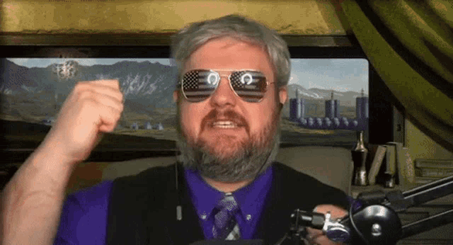 a man in a purple shirt and tie wearing sunglasses with an american flag on them