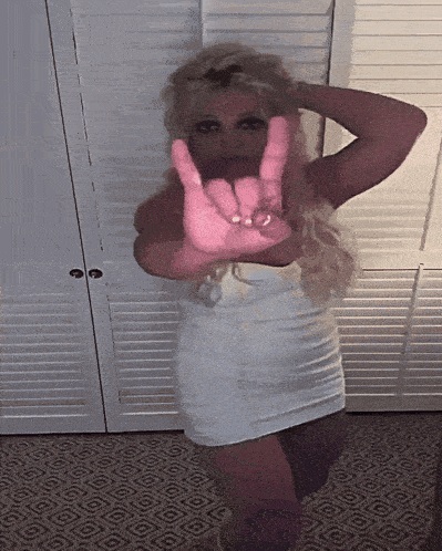a woman in a white dress is making a hand gesture