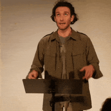 a man in a green jacket stands at a podium with his hands outstretched