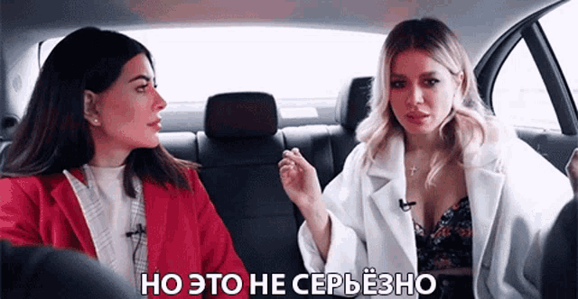 two women are sitting in the back seat of a car and one of them is wearing a white coat